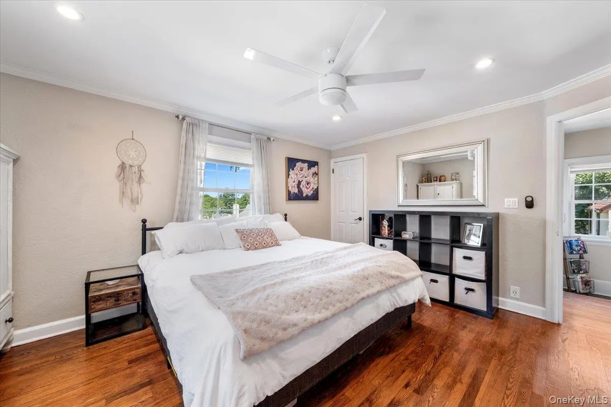 Bedroom featuring wood-finish flooring, a ceiling fan with integrated lighting, recessed lighting, crown molding, and two windows with white trim Bedroom featuring wood-finish flooring, a ceiling fan with integrated lighting, recessed lighting, crown molding, and two windows with white trim