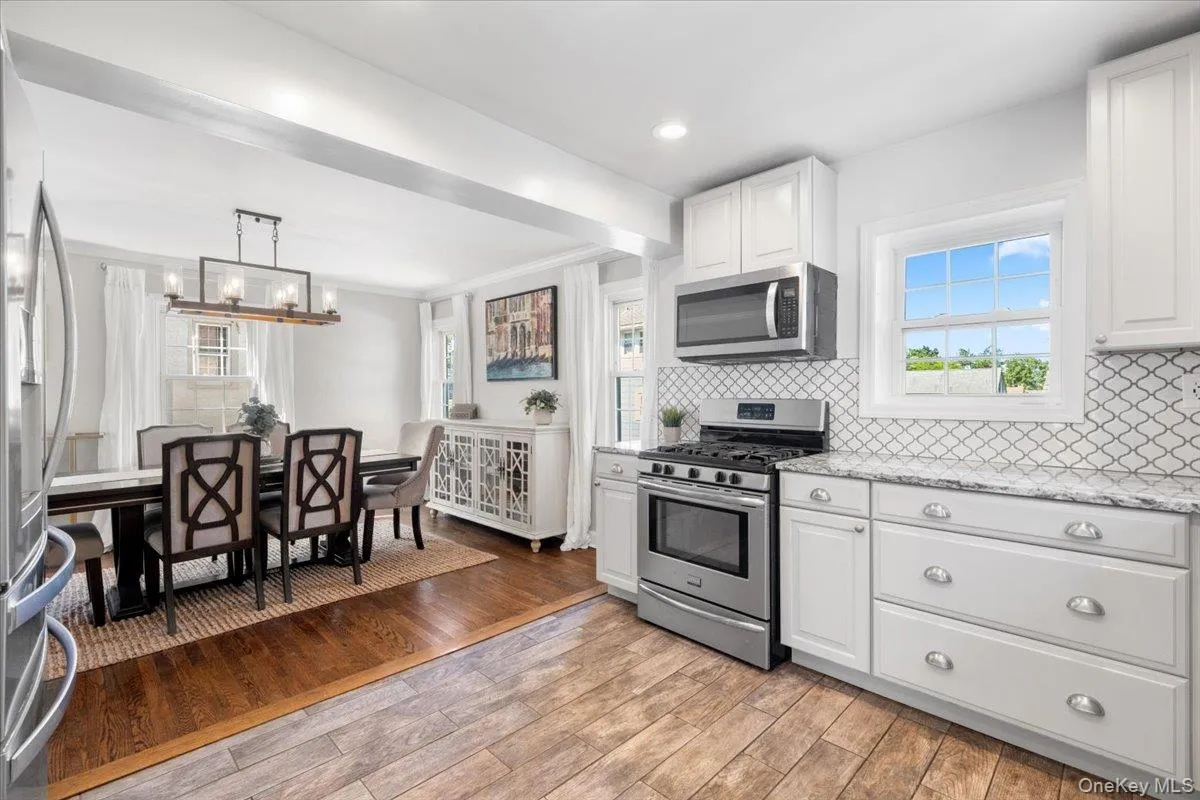 Open-concept kitchen and dining area featuring white cabinetry, stainless steel appliances, and wood-finish flooring Open-concept kitchen and dining area featuring white cabinetry, stainless steel appliances, and wood-finish flooring