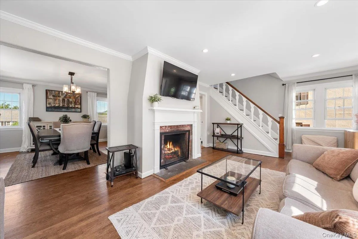 Living room with wood-finish flooring, a fireplace featuring a stone surround, and a classic white mantel. And view of stairs to bedrooms and view of dining room Living room with wood-finish flooring, a fireplace featuring a stone surround, and a classic white mantel. And view of stairs to bedrooms and view of dining room