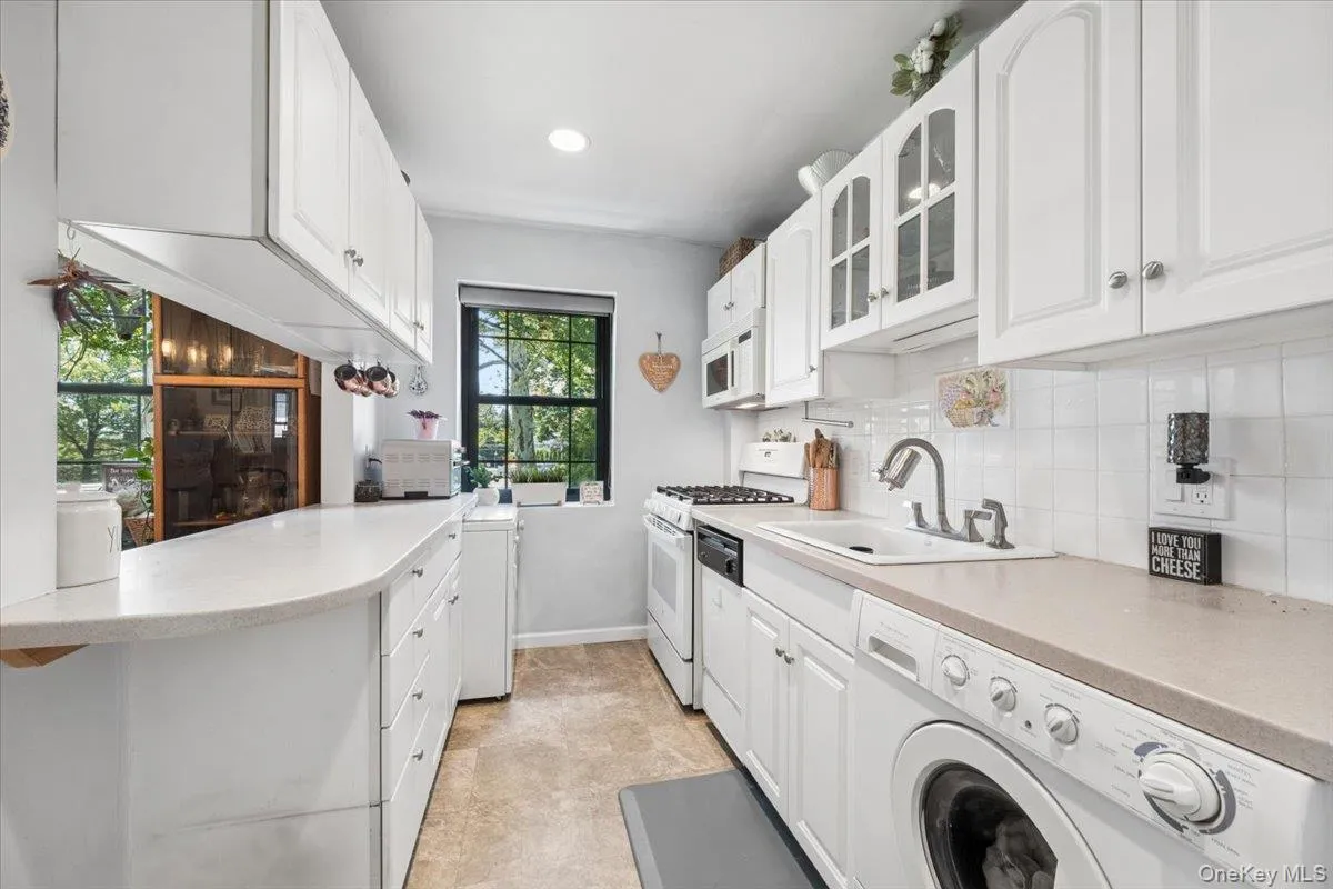 Galley kitchen featuring white cabinetry, light-toned countertops, and a tile backsplash - Washer & dryer too! Galley kitchen featuring white cabinetry, light-toned countertops, and a tile backsplash - Washer & dryer too!