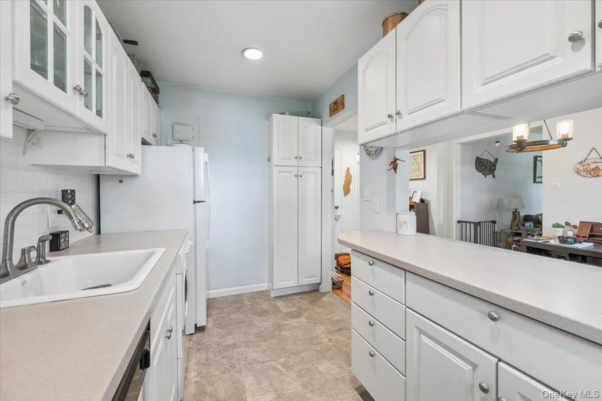 Kitchen featuring white cabinetry with silver hardware, light-toned countertops, and a white sink with a gooseneck faucet Kitchen featuring white cabinetry with silver hardware, light-toned countertops, and a white sink with a gooseneck faucet