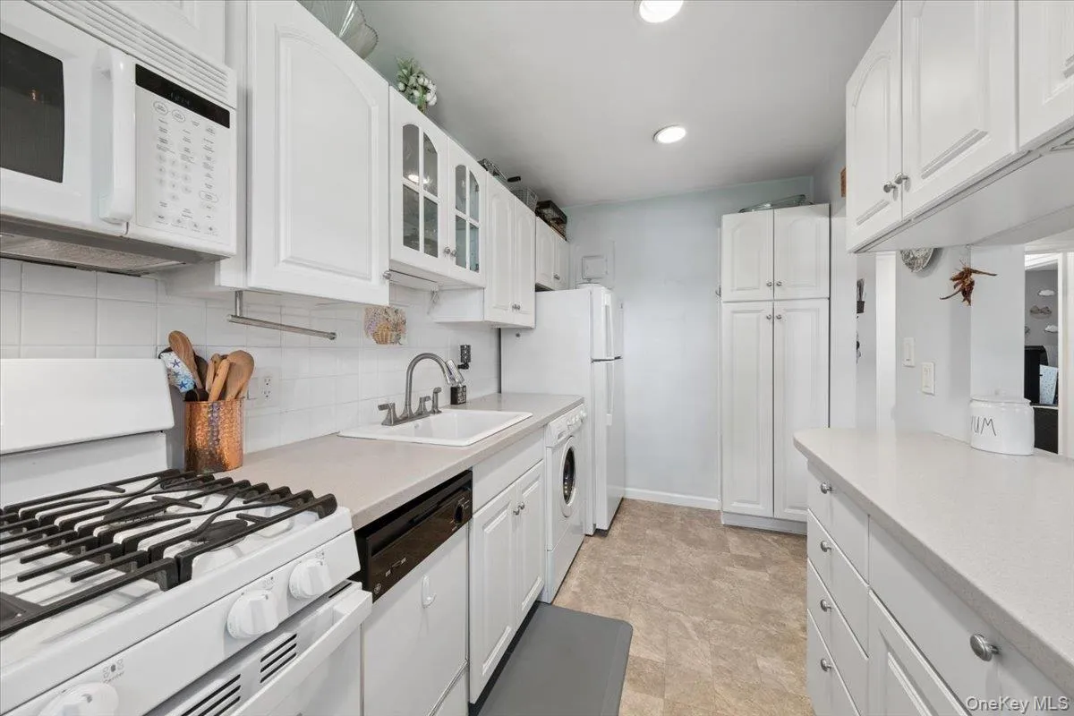 Kitchen featuring extensive white cabinetry, a built-in gas range with an overhead microwave, a white ceramic sink, and neutral countertops Kitchen featuring extensive white cabinetry, a built-in gas range with an overhead microwave, a white ceramic sink, and neutral countertops