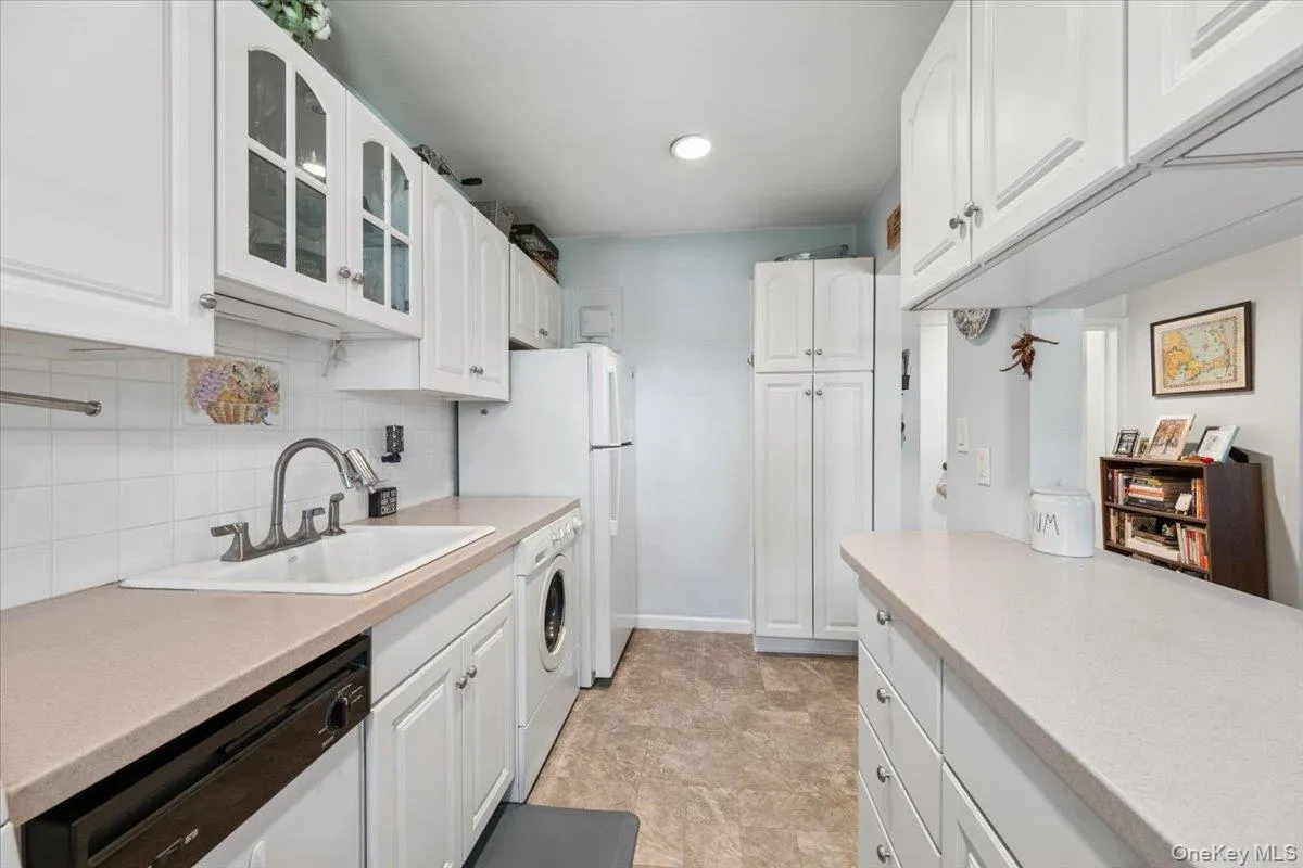 Galley kitchen featuring white cabinetry, light-toned countertops, and tile flooring Galley kitchen featuring white cabinetry, light-toned countertops, and tile flooring