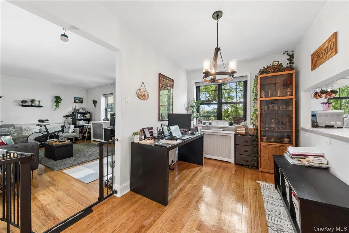 Dining area currently being used as an at-home-office featuring wood-finish flooring, a contemporary chandelier, and a large window with dark trim Dining area currently being used as an at-home-office featuring wood-finish flooring, a contemporary chandelier, and a large window with dark trim