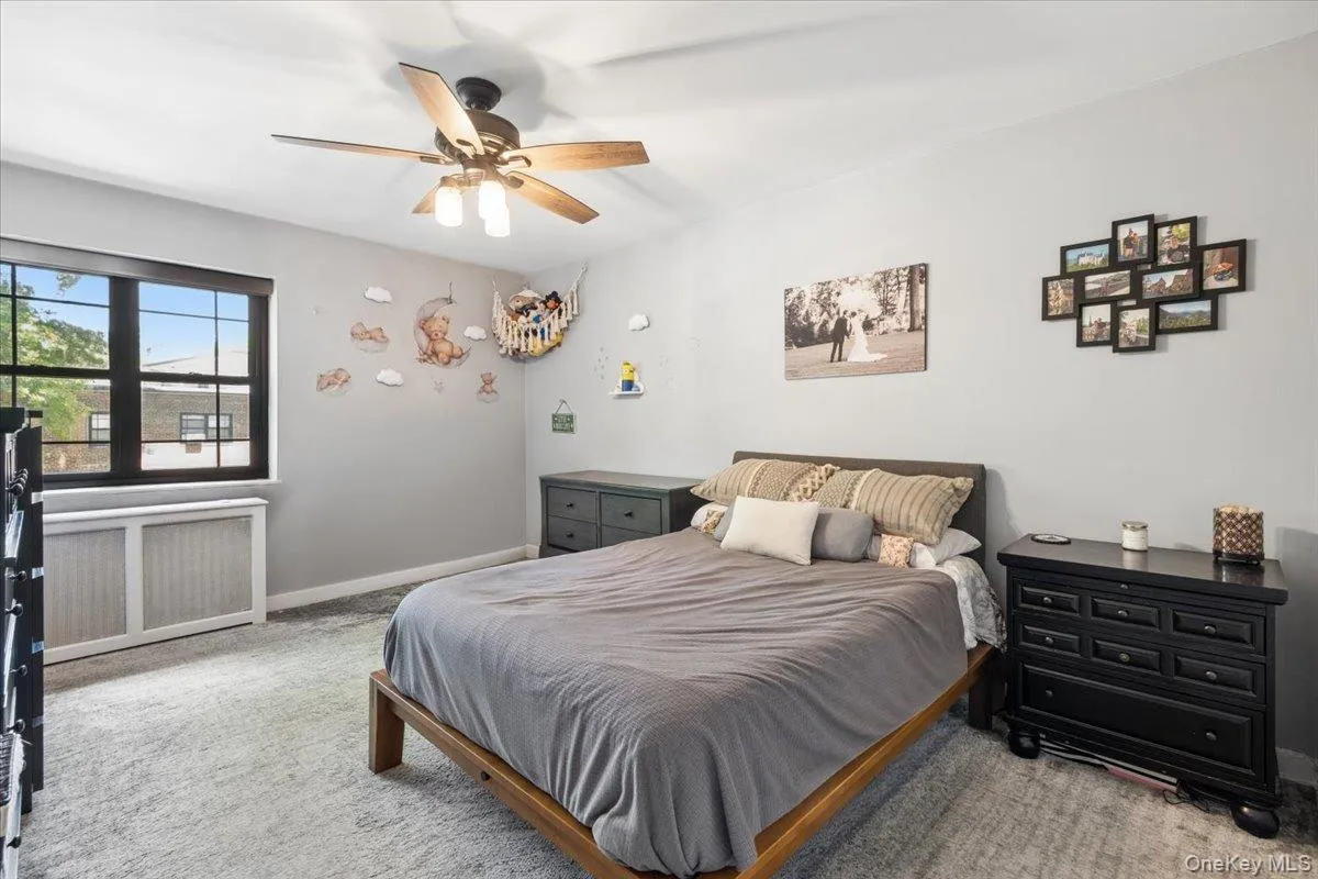 Carpeted bedroom featuring a ceiling fan with light fixture, a window with dark framing Carpeted bedroom featuring a ceiling fan with light fixture, a window with dark framing