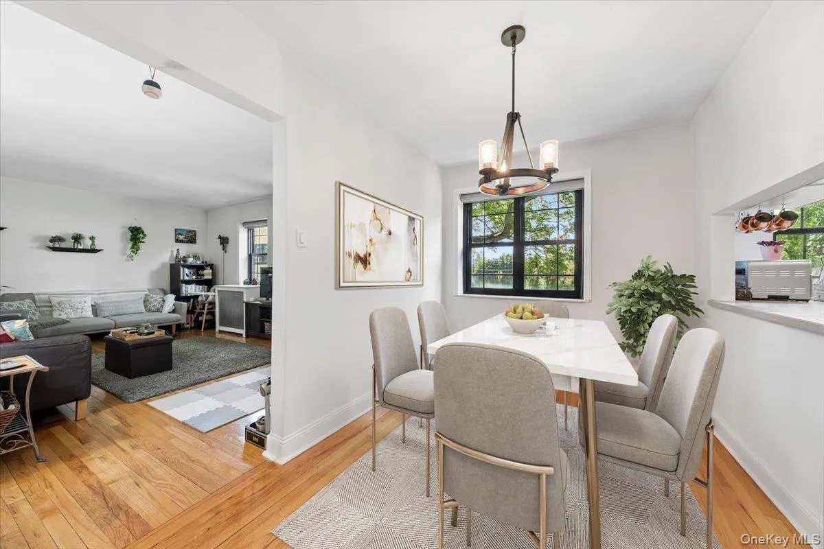 Dining area featuring a contemporary chandelier, a pass-through window to the kitchen, and a window with outdoor greenery (Virtually Staged) Dining area featuring a contemporary chandelier, a pass-through window to the kitchen, and a window with outdoor greenery (Virtually Staged)
