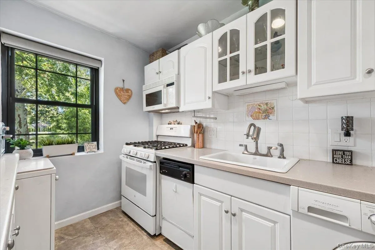 Kitchen featuring white cabinetry, a gas range, white tile backsplash, and a window with exterior views Kitchen featuring white cabinetry, a gas range, white tile backsplash, and a window with exterior views