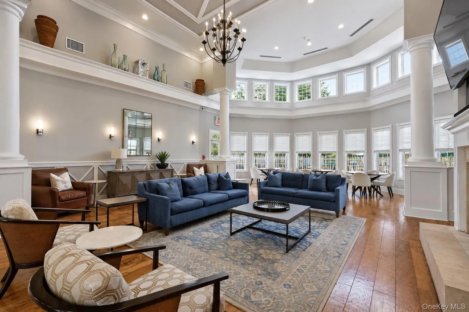 Spacious communal area in clubhouse featuring comfortable seating, a coffered ceiling with a prominent chandelier, television, and fireplace. Spacious communal area in clubhouse featuring comfortable seating, a coffered ceiling with a prominent chandelier, television, and fireplace.