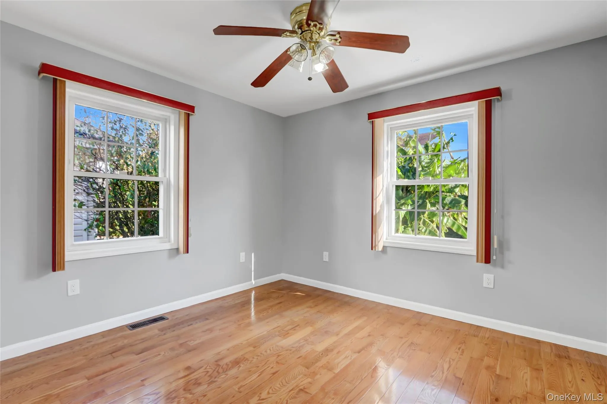 wood-finish flooring, light gray walls, and two large windows with red and cream valances wood-finish flooring, light gray walls, and two large windows with red and cream valances