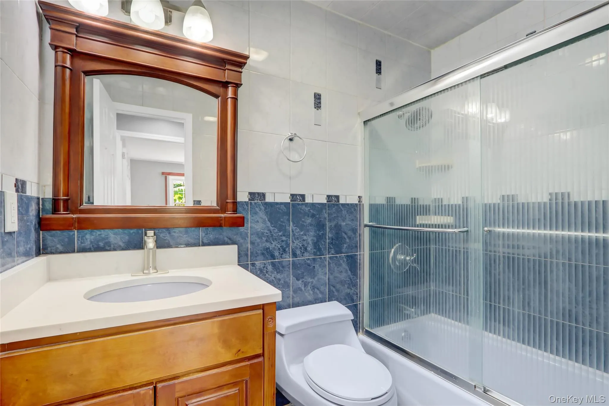 1st Floor Bathroom featuring a wood-finish vanity with a light-colored countertop, an undermount sink, and a framed mirror 1st Floor Bathroom featuring a wood-finish vanity with a light-colored countertop, an undermount sink, and a framed mirror