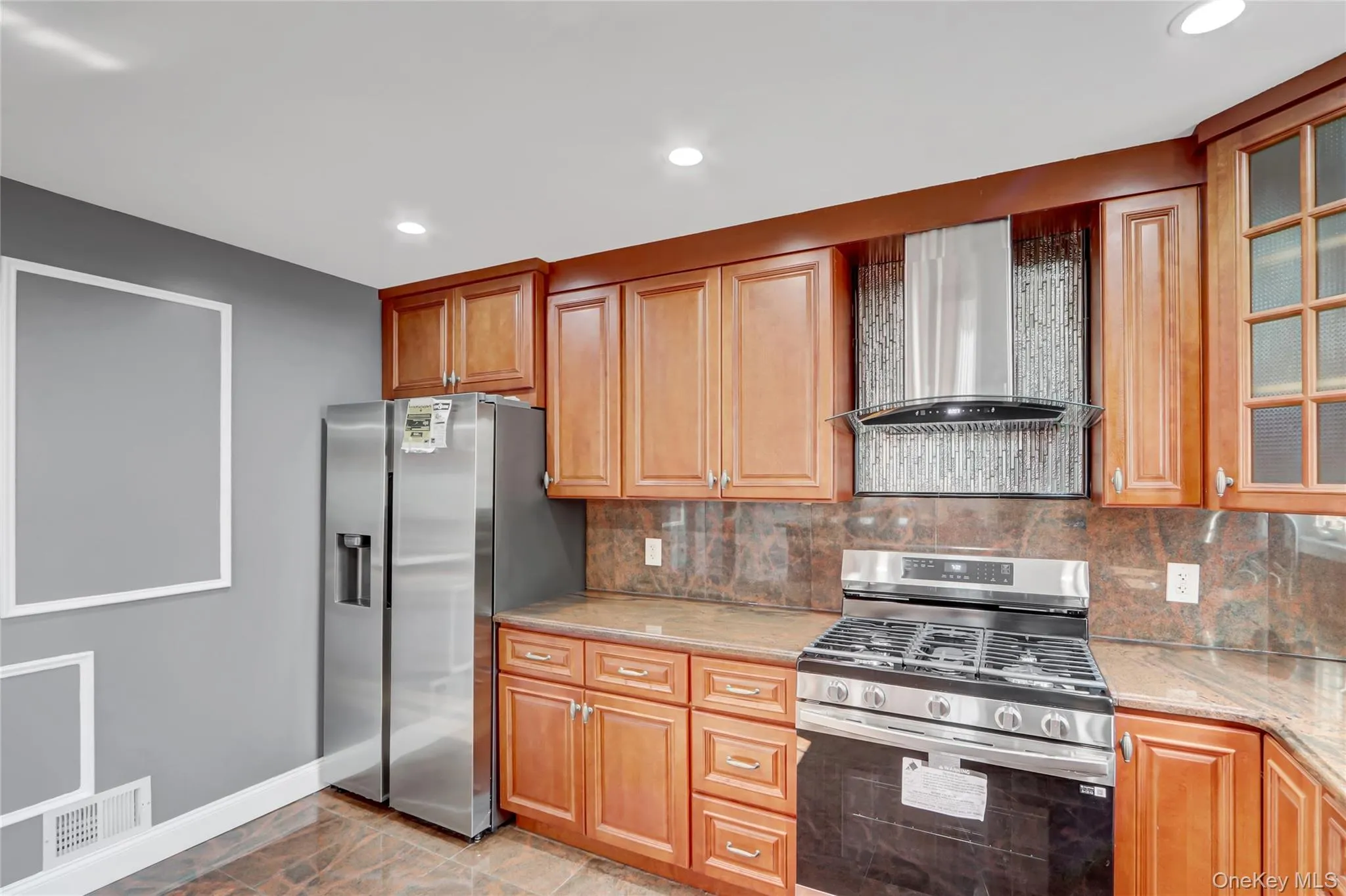 Kitchen featuring stainless steel appliances, wood cabinetry, stone countertops, and tiled backsplash Kitchen featuring stainless steel appliances, wood cabinetry, stone countertops, and tiled backsplash
