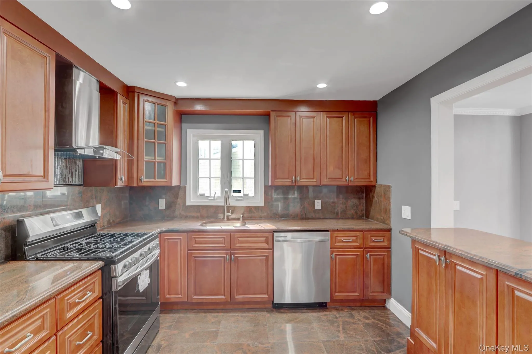 Kitchen featuring wood cabinetry with select glass-front doors, stone countertops, and a full tile backsplash. Kitchen featuring wood cabinetry with select glass-front doors, stone countertops, and a full tile backsplash.