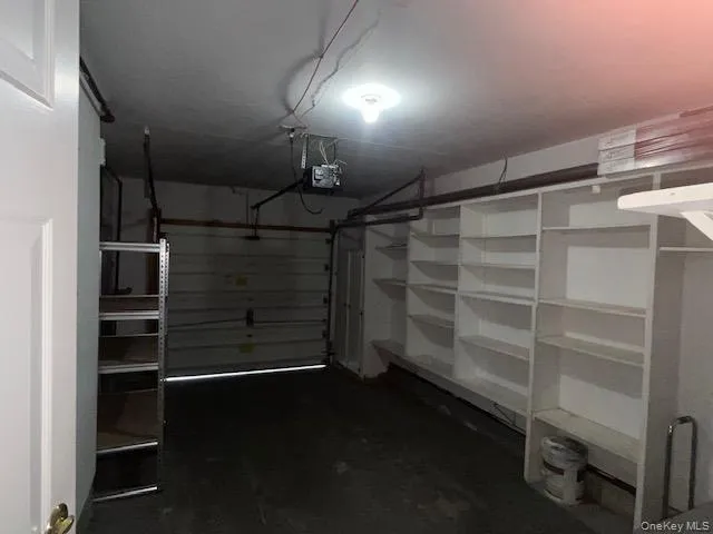 Garage interior with ample built-in shelving, concrete flooring, and an overhead garage door mechanism Garage interior with ample built-in shelving, concrete flooring, and an overhead garage door mechanism