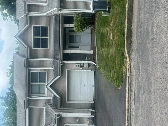Two-story townhome featuring neutral-toned siding, an attached garage, and a paved driveway Two-story townhome featuring neutral-toned siding, an attached garage, and a paved driveway