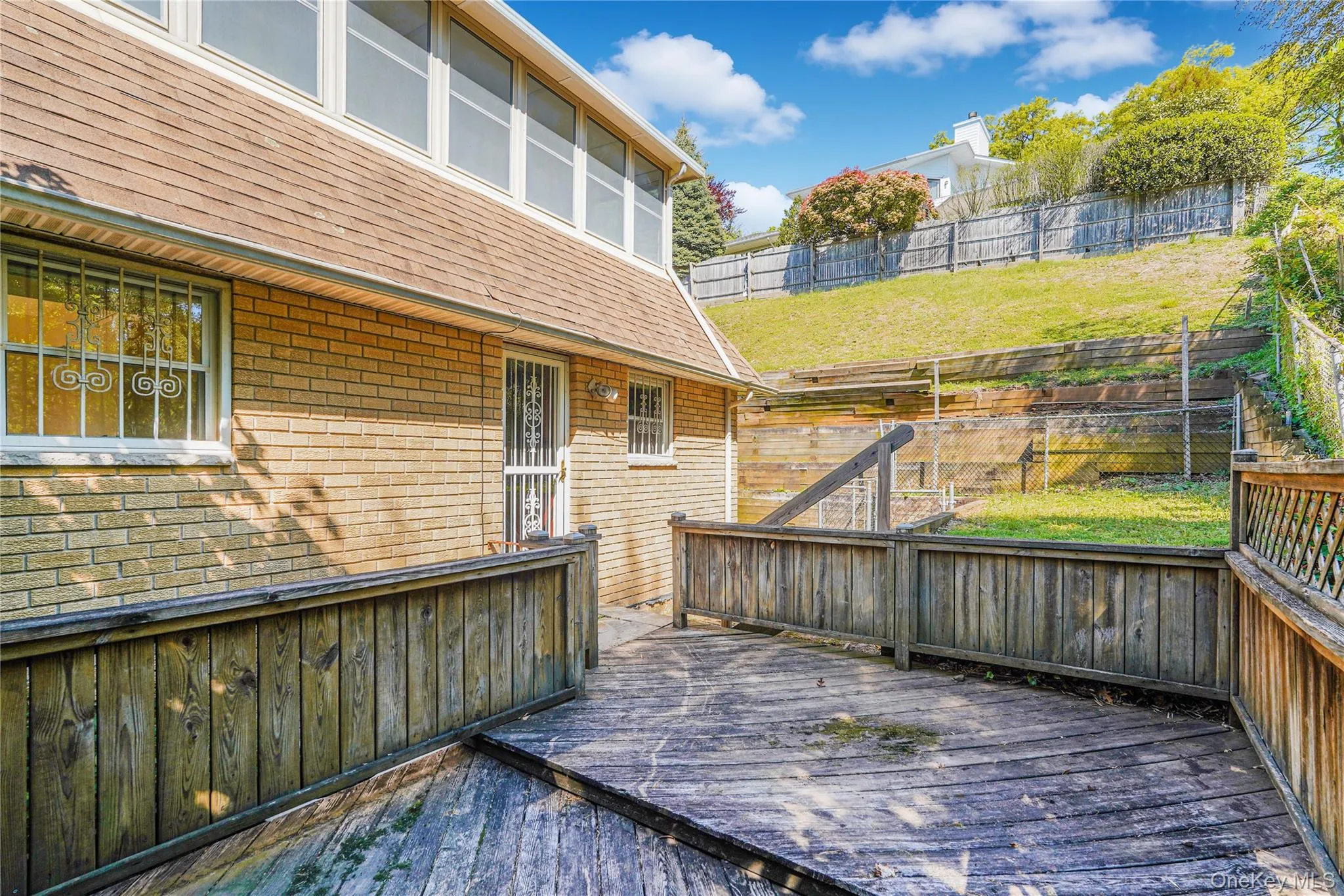 Expansive multi-level wood deck with wood railings, offering a terraced backyard featuring a sloped lawn and a wood privacy fence Expansive multi-level wood deck with wood railings, offering a terraced backyard featuring a sloped lawn and a wood privacy fence