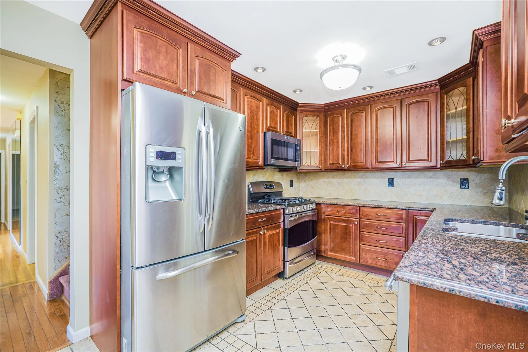Kitchen featuring abundant wood cabinetry, stainless steel appliances including a refrigerator and range, granite-finish countertops, and a tiled backsplash Kitchen featuring abundant wood cabinetry, stainless steel appliances including a refrigerator and range, granite-finish countertops, and a tiled backsplash