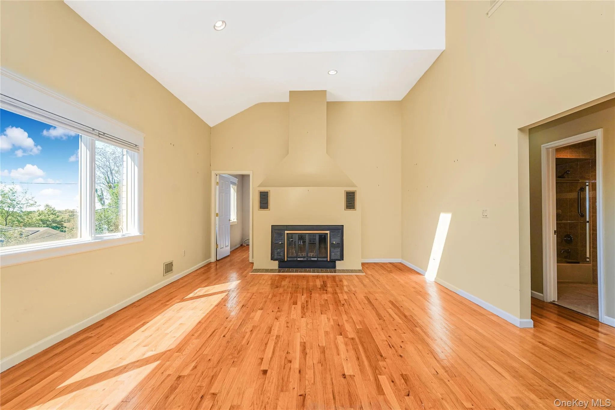 Open-concept living space featuring wood-finish flooring, a vaulted ceiling, and a prominent fireplace with a dark surround Open-concept living space featuring wood-finish flooring, a vaulted ceiling, and a prominent fireplace with a dark surround