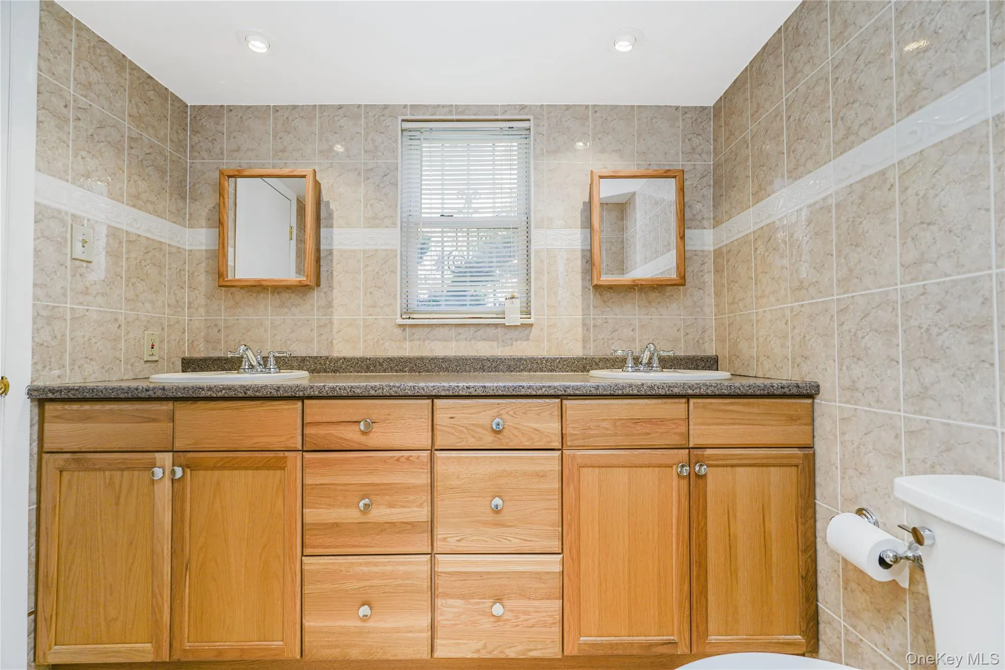 Bathroom featuring a dual vanity with light wood cabinetry, a dark countertop, and integrated sinks Bathroom featuring a dual vanity with light wood cabinetry, a dark countertop, and integrated sinks