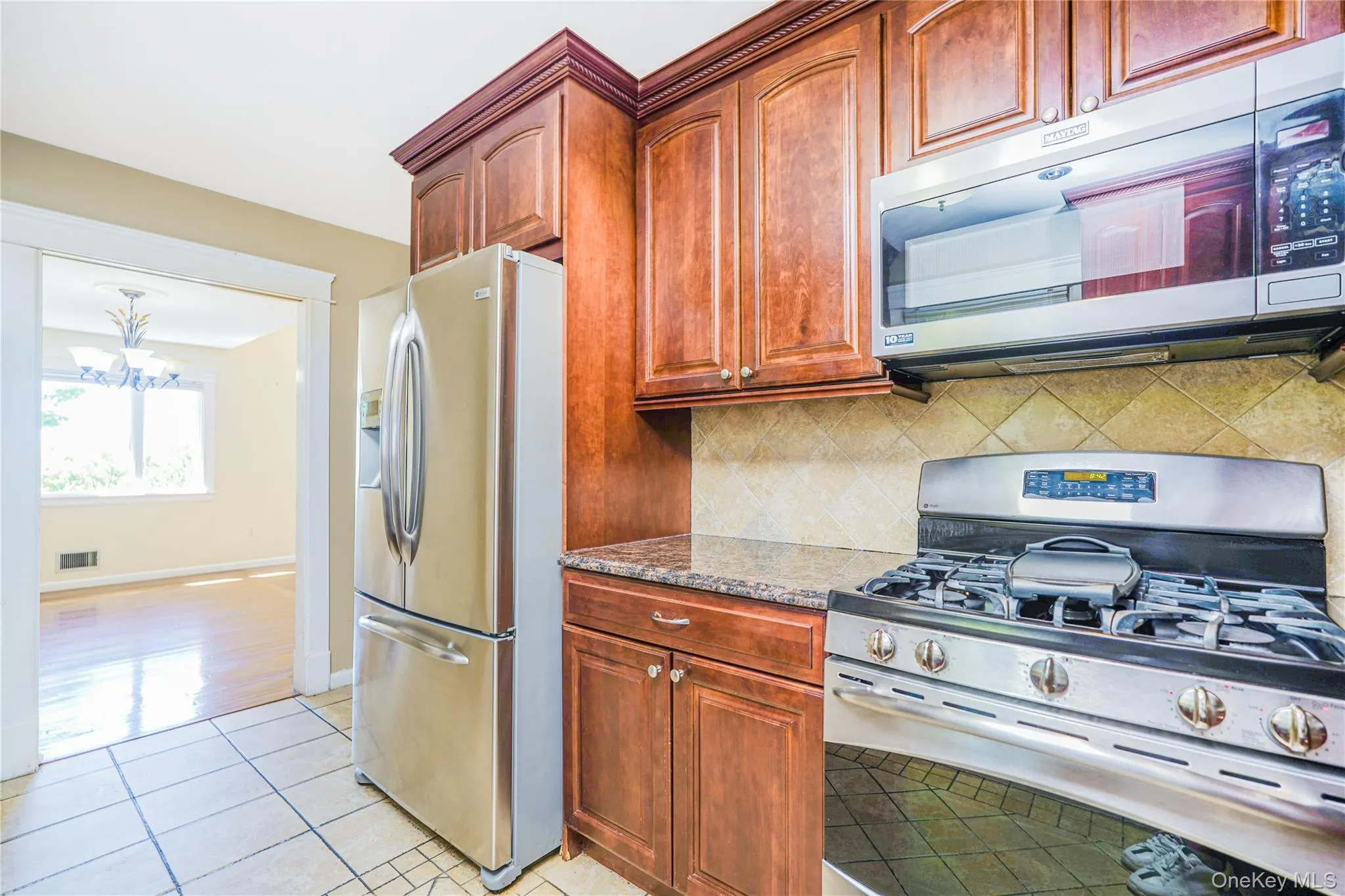 Kitchen featuring warm wood cabinetry, stainless steel appliances, a gas range, a tile backsplash, and a granite-style countertop Kitchen featuring warm wood cabinetry, stainless steel appliances, a gas range, a tile backsplash, and a granite-style countertop