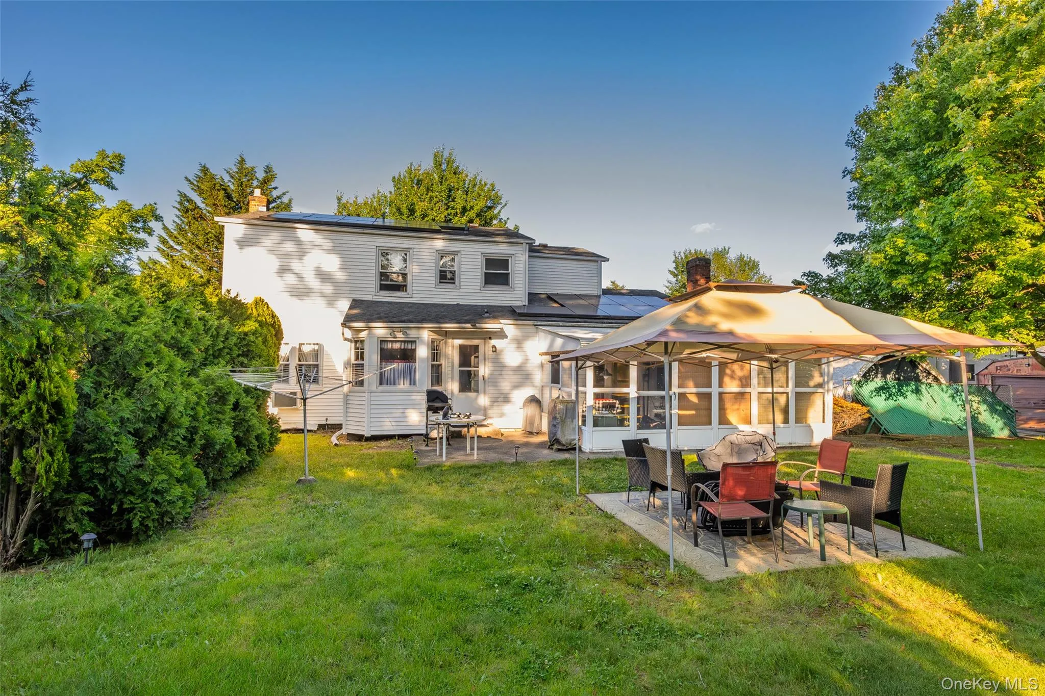Spacious rear yard with an expansive lawn, established mature trees, and a concrete patio area Spacious rear yard with an expansive lawn, established mature trees, and a concrete patio area