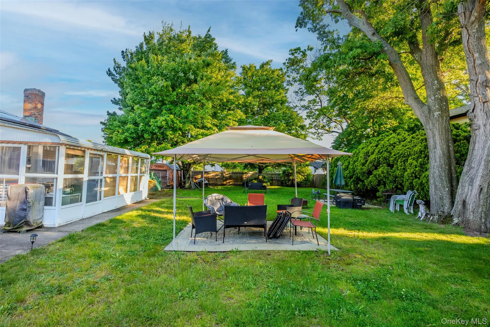 Large yard with mature trees and a sunroom extension featuring multiple windows, a chimney, and a patio area Large yard with mature trees and a sunroom extension featuring multiple windows, a chimney, and a patio area
