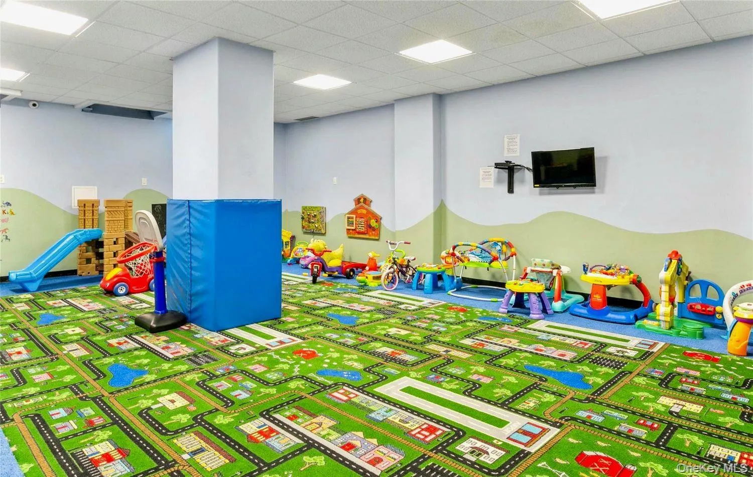 Recreational room featuring a durable patterned carpet, light blue walls with a green accent mural, recessed ceiling lighting, and a wall-mounted television Recreational room featuring a durable patterned carpet, light blue walls with a green accent mural, recessed ceiling lighting, and a wall-mounted television