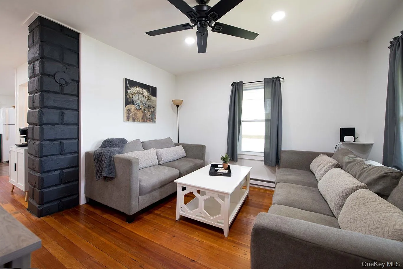Hardwood flooring throughout a living space featuring a black ceiling fan with integrated lighting, recessed ceiling lighting, and a prominent dark-toned brick-look architectural column Hardwood flooring throughout a living space featuring a black ceiling fan with integrated lighting, recessed ceiling lighting, and a prominent dark-toned brick-look architectural column