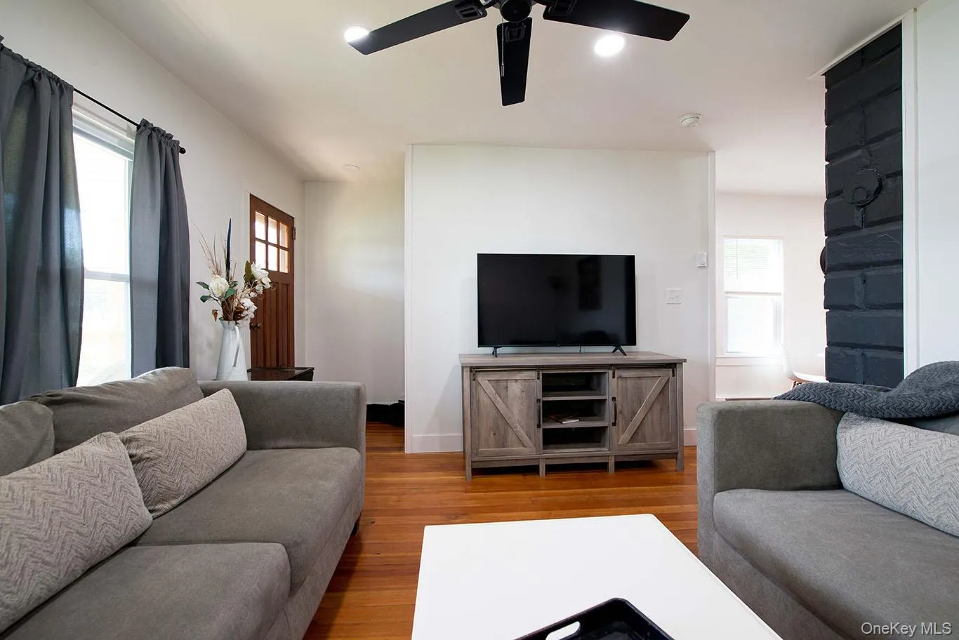 Living area featuring hardwood flooring, a black ceiling fan, recessed lighting, a paneled entry door, and an exposed brick accent wall Living area featuring hardwood flooring, a black ceiling fan, recessed lighting, a paneled entry door, and an exposed brick accent wall