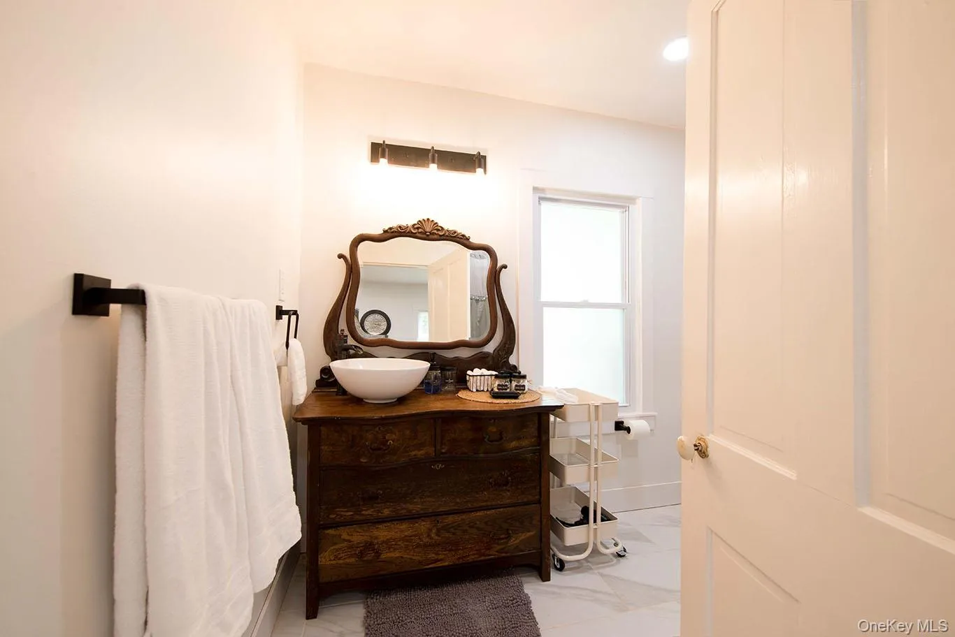 Bathroom featuring a wood-finish vanity with a vessel sink, an ornate framed mirror, and a frosted window Bathroom featuring a wood-finish vanity with a vessel sink, an ornate framed mirror, and a frosted window