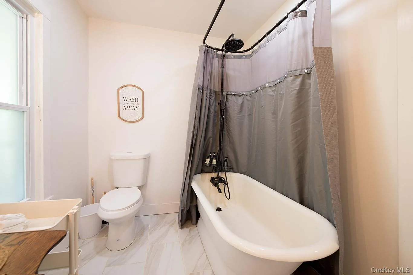 Bathroom featuring a white freestanding bathtub with a black shower fixture, white toilet, and white tile flooring Bathroom featuring a white freestanding bathtub with a black shower fixture, white toilet, and white tile flooring