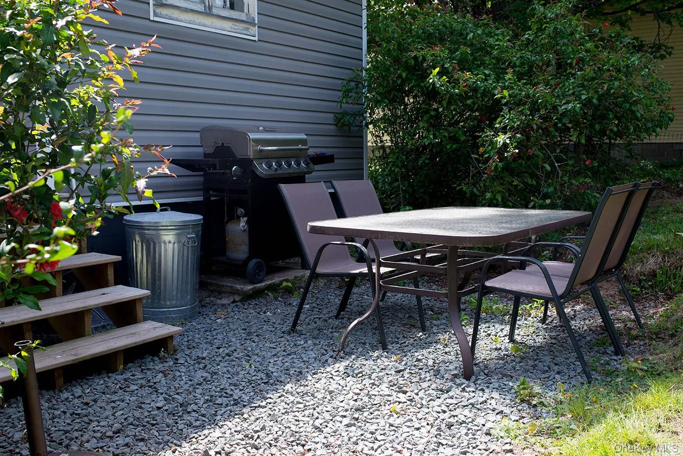 Gravel patio area featuring a nice area for outdoor dining with natural foliage, and beautiful bushes. Gravel patio area featuring a nice area for outdoor dining with natural foliage, and beautiful bushes.