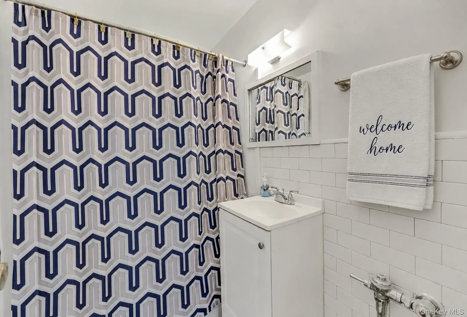 Bathroom featuring white subway tile wainscoting, a wall-mounted vanity with a porcelain sink, a framed medicine cabinet, and a chrome light fixture Bathroom featuring white subway tile wainscoting, a wall-mounted vanity with a porcelain sink, a framed medicine cabinet, and a chrome light fixture
