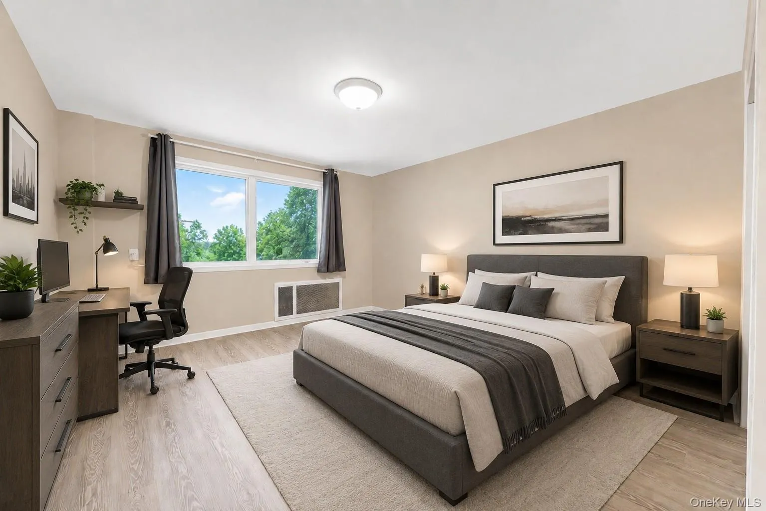 Spacious bedroom featuring light wood-finish flooring, a large window, neutral wall tones, and a built-in heating/cooling unit Spacious bedroom featuring light wood-finish flooring, a large window, neutral wall tones, and a built-in heating/cooling unit
