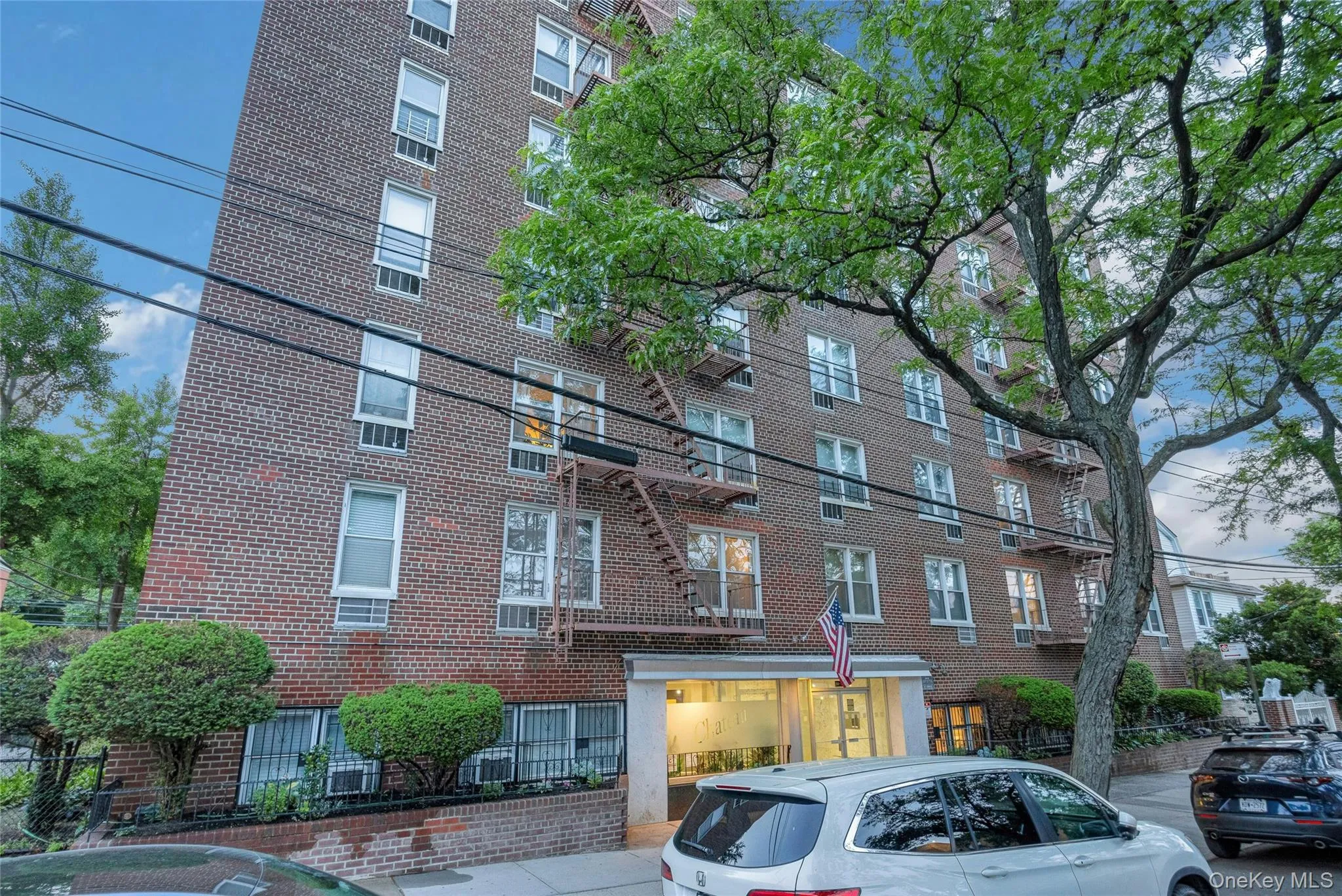 Brick facade multi-story building featuring multiple windows, a prominent entrance, exterior fire escapes, and mature trees Brick facade multi-story building featuring multiple windows, a prominent entrance, exterior fire escapes, and mature trees