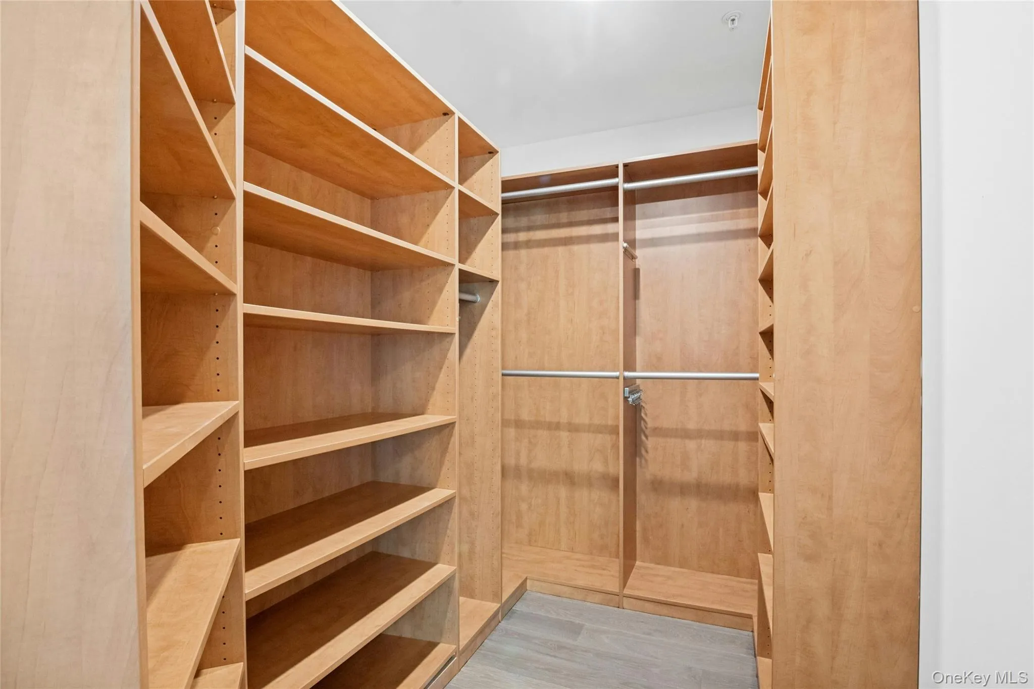 Custom closet system featuring light wood-finish shelving, multiple hanging rods, and integrated shoe storage and dimmable overhead lighting Custom closet system featuring light wood-finish shelving, multiple hanging rods, and integrated shoe storage and dimmable overhead lighting
