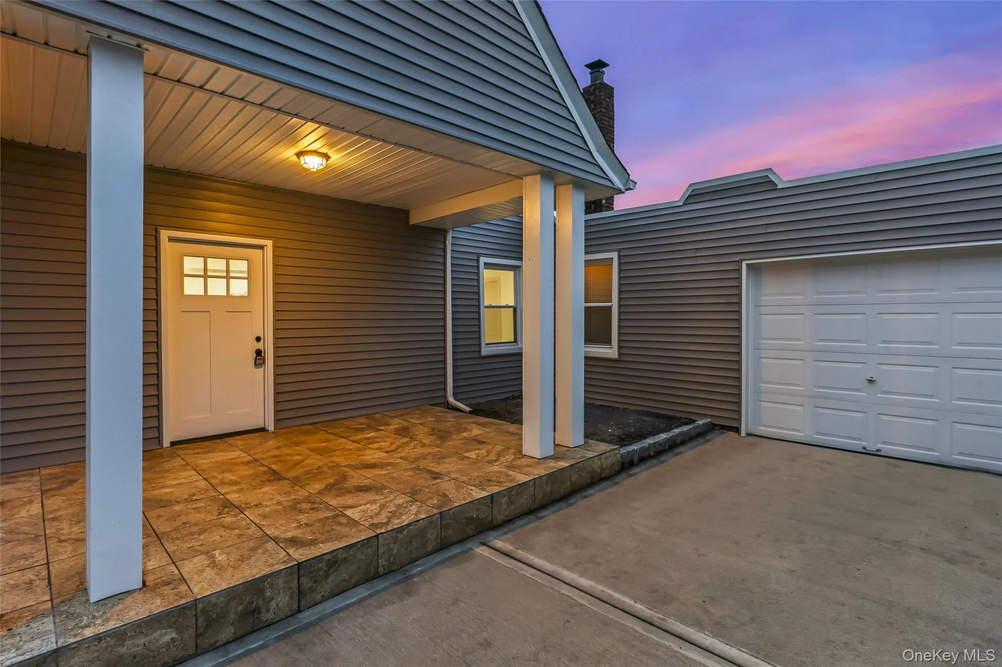 Doorway to property featuring a patio area, a chimney, concrete driveway, and an attached garage Doorway to property featuring a patio area, a chimney, concrete driveway, and an attached garage