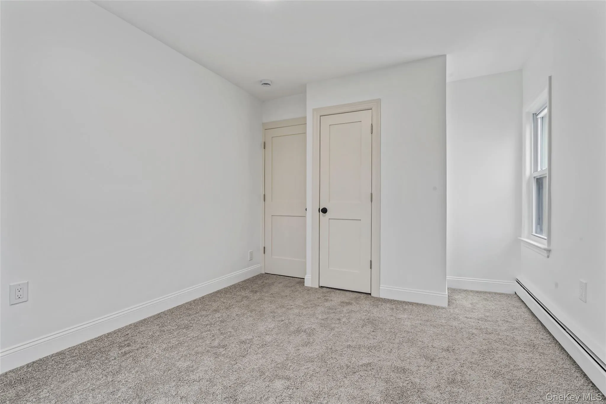 Unfurnished bedroom featuring baseboard heating and light colored carpet Unfurnished bedroom featuring baseboard heating and light colored carpet