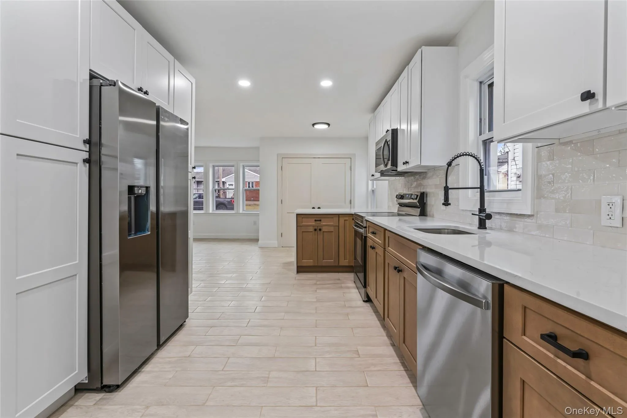 Kitchen with appliances with stainless steel finishes, brown cabinets, recessed lighting, light stone counters, and white cabinetry Kitchen with appliances with stainless steel finishes, brown cabinets, recessed lighting, light stone counters, and white cabinetry