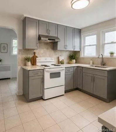 Kitchen featuring grey cabinetry, light countertops, and a tile backsplash Kitchen featuring grey cabinetry, light countertops, and a tile backsplash