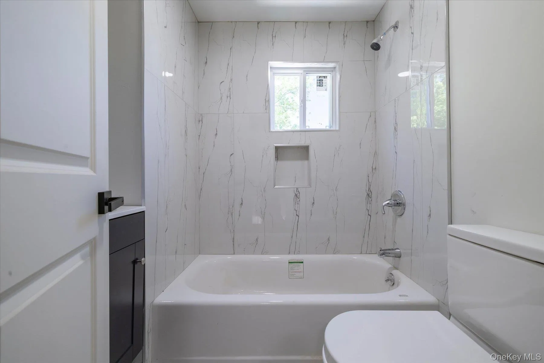 Tub and shower combination with white marble-look tile surround and chrome fixtures Tub and shower combination with white marble-look tile surround and chrome fixtures
