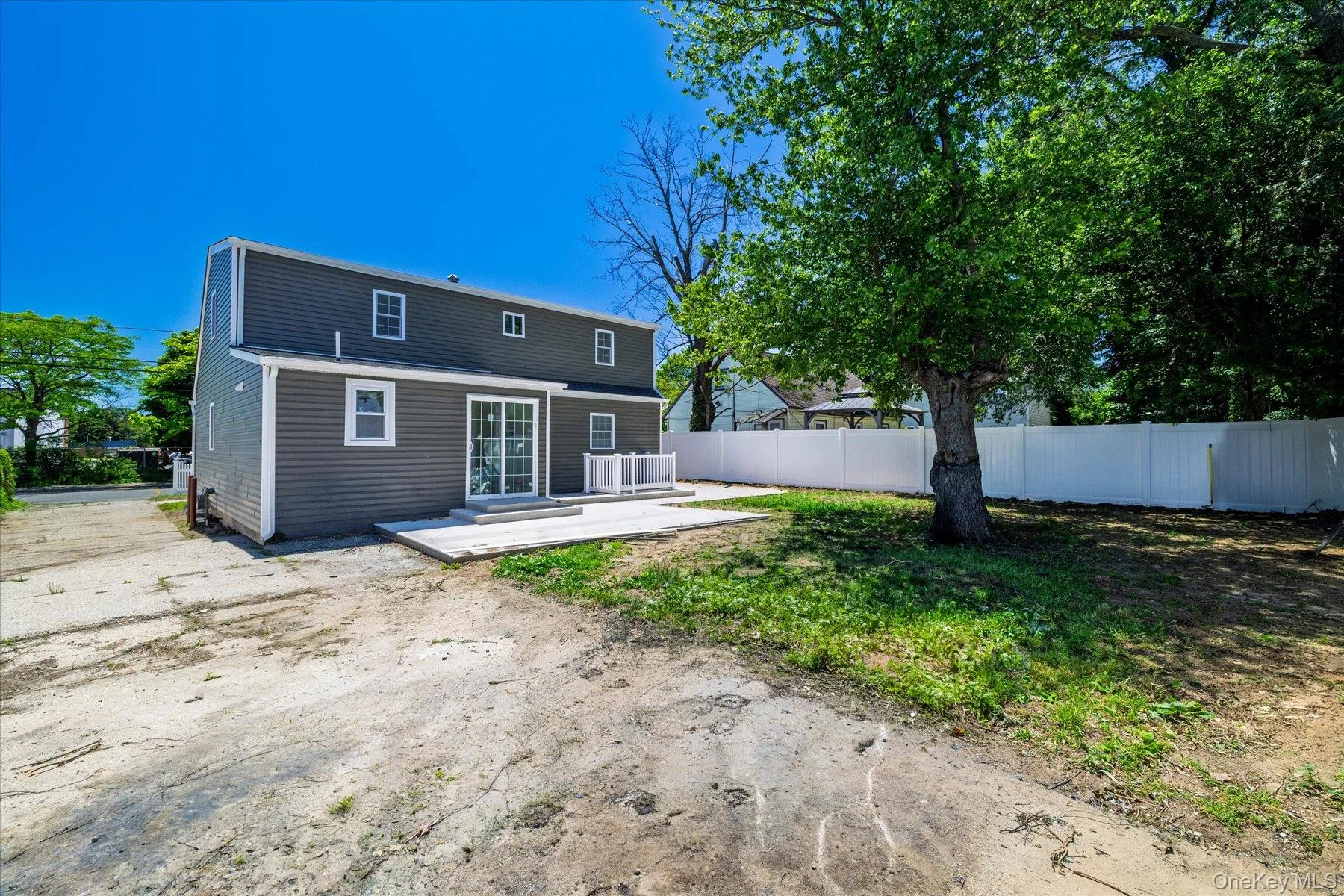 Rear exterior featuring gray horizontal siding, white trim, sliding glass patio doors, and an expansive concrete patio Rear exterior featuring gray horizontal siding, white trim, sliding glass patio doors, and an expansive concrete patio