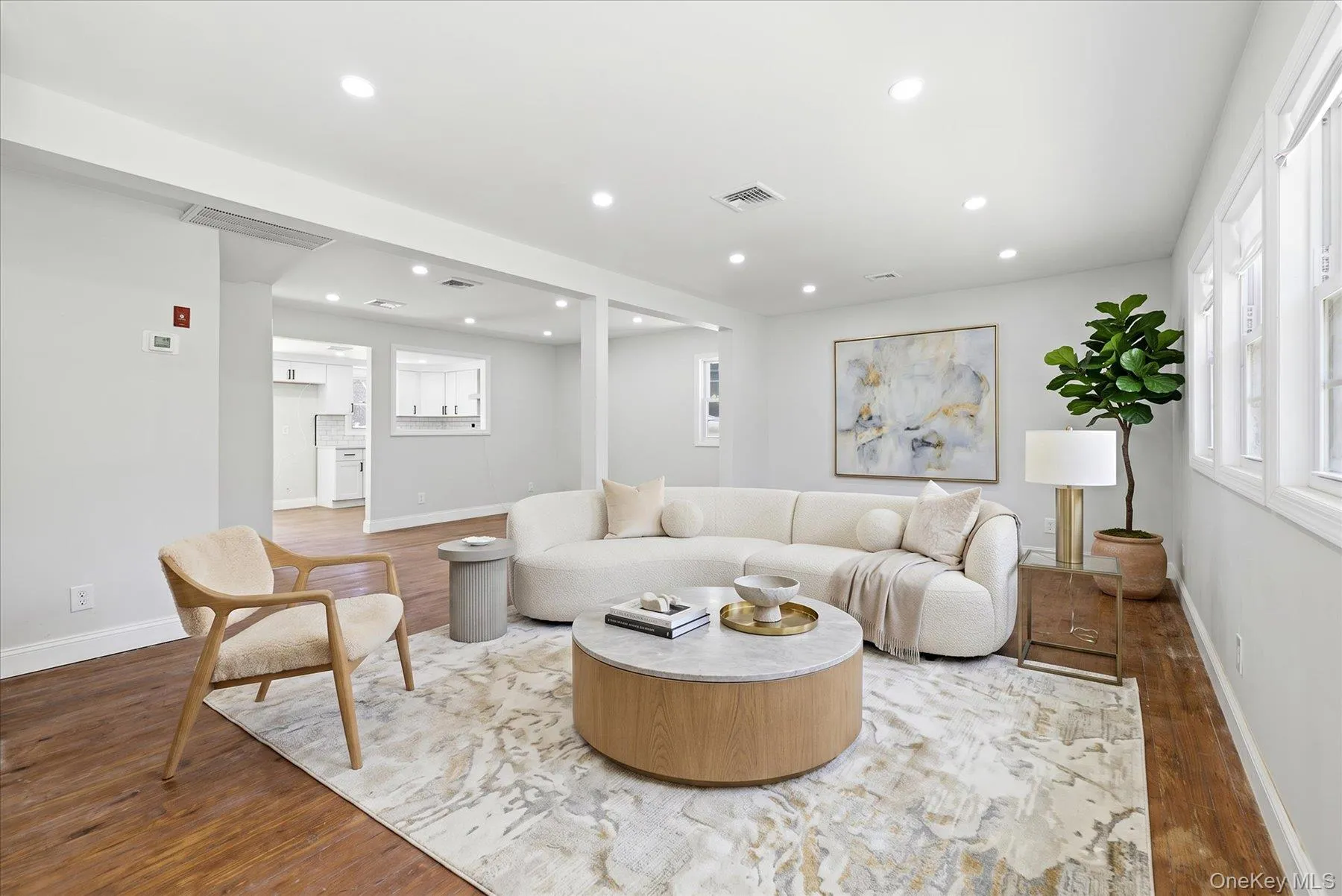 Spacious living area featuring wood-finish flooring, recessed lighting, multiple windows, and a structured opening to the kitchen Spacious living area featuring wood-finish flooring, recessed lighting, multiple windows, and a structured opening to the kitchen