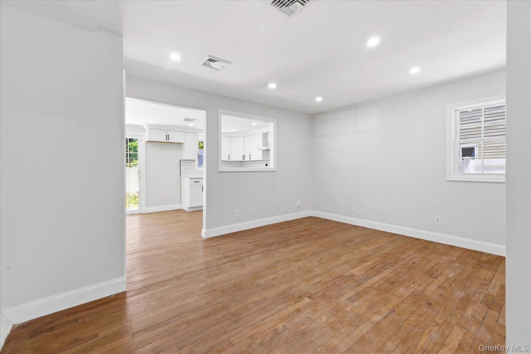 Spacious room featuring wood-finish flooring, recessed lighting, and white baseboards Spacious room featuring wood-finish flooring, recessed lighting, and white baseboards