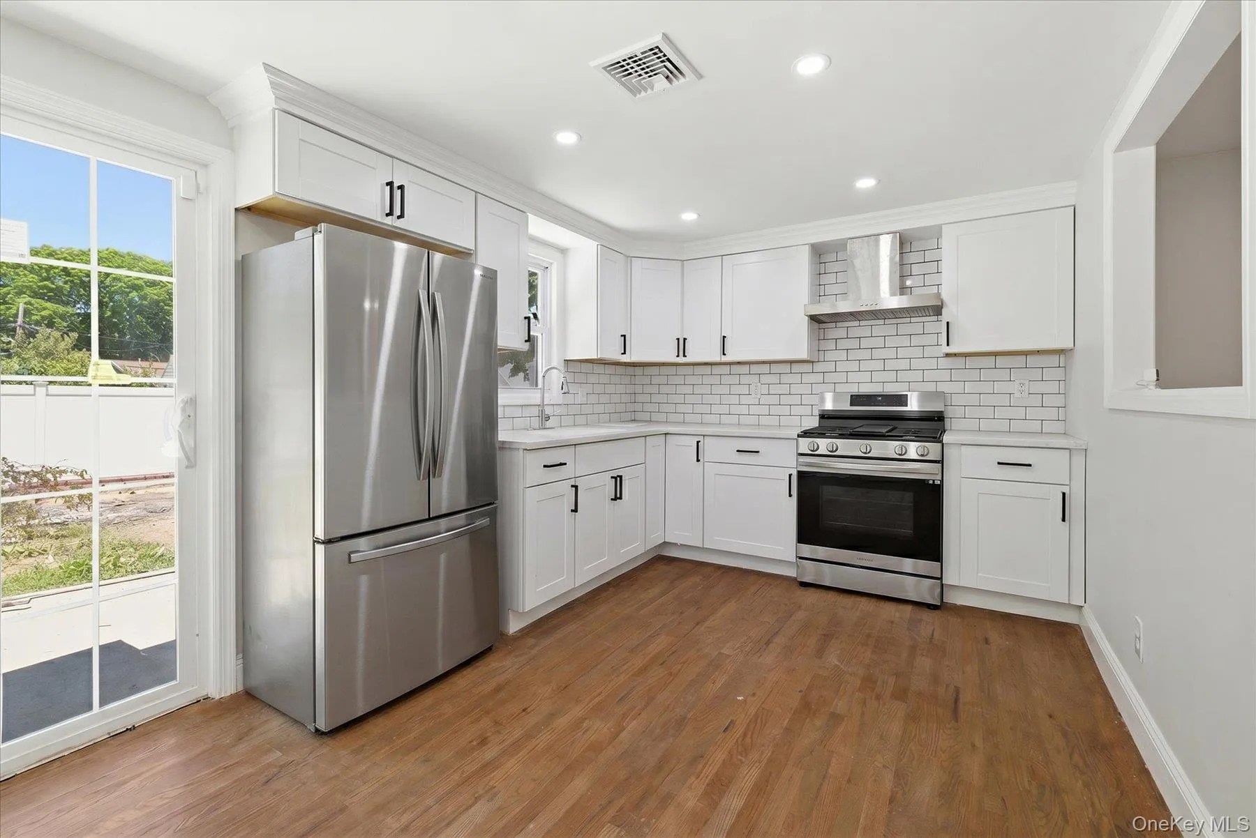 Kitchen featuring white shaker cabinetry, stainless steel appliances, subway tile backsplash, and wood-finish flooring Kitchen featuring white shaker cabinetry, stainless steel appliances, subway tile backsplash, and wood-finish flooring