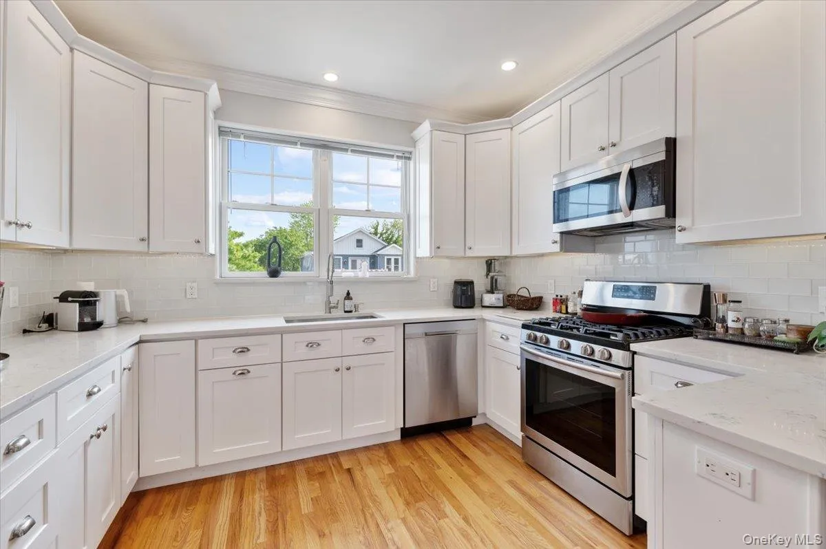 Kitchen with stainless steel appliances, white cabinets, crown molding, backsplash, and light wood-type flooring Kitchen with stainless steel appliances, white cabinets, crown molding, backsplash, and light wood-type flooring