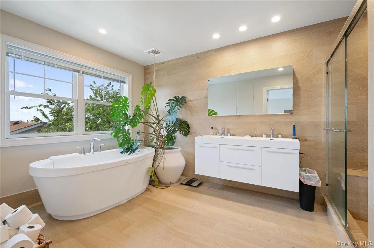 Full bath with double vanity, a freestanding tub, a stall shower, recessed lighting, and wood finished floors Full bath with double vanity, a freestanding tub, a stall shower, recessed lighting, and wood finished floors