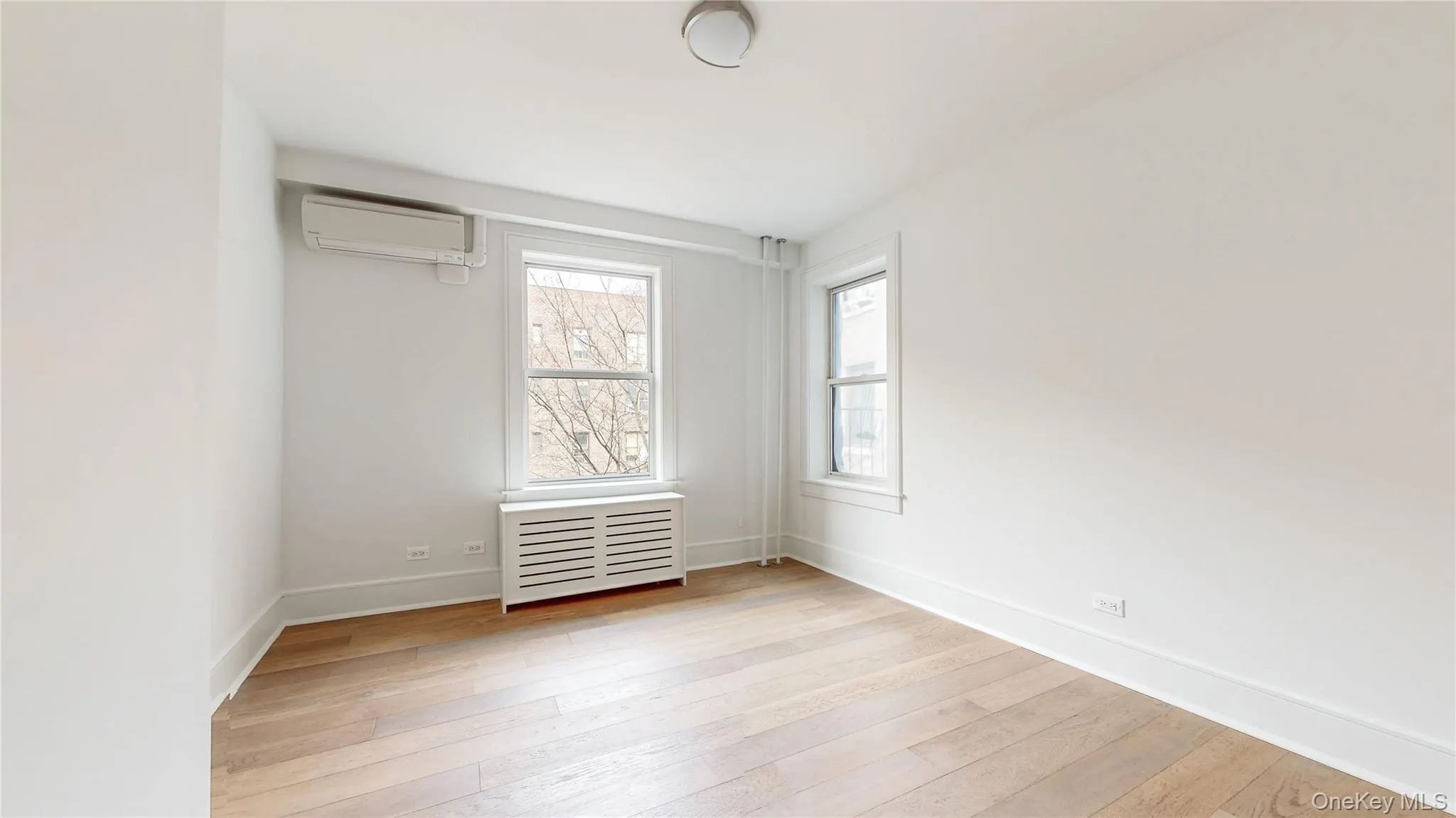 Bright bedroom featuring two double-hung windows, wood-finish flooring, and white painted walls Bright bedroom featuring two double-hung windows, wood-finish flooring, and white painted walls