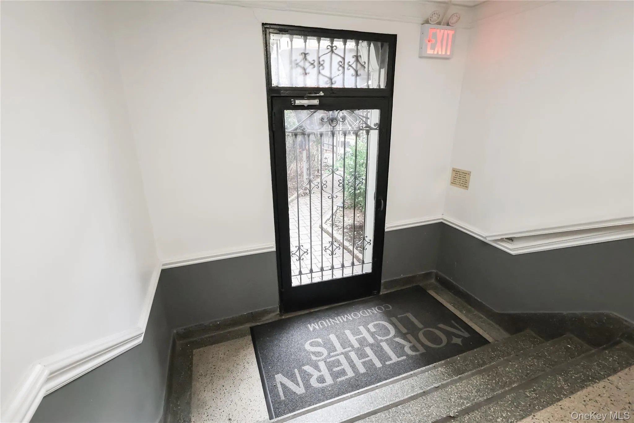 Entryway featuring a security door with decorative wrought ironwork, painted white walls with a dark grey wainscoting, and durable terrazzo flooring Entryway featuring a security door with decorative wrought ironwork, painted white walls with a dark grey wainscoting, and durable terrazzo flooring