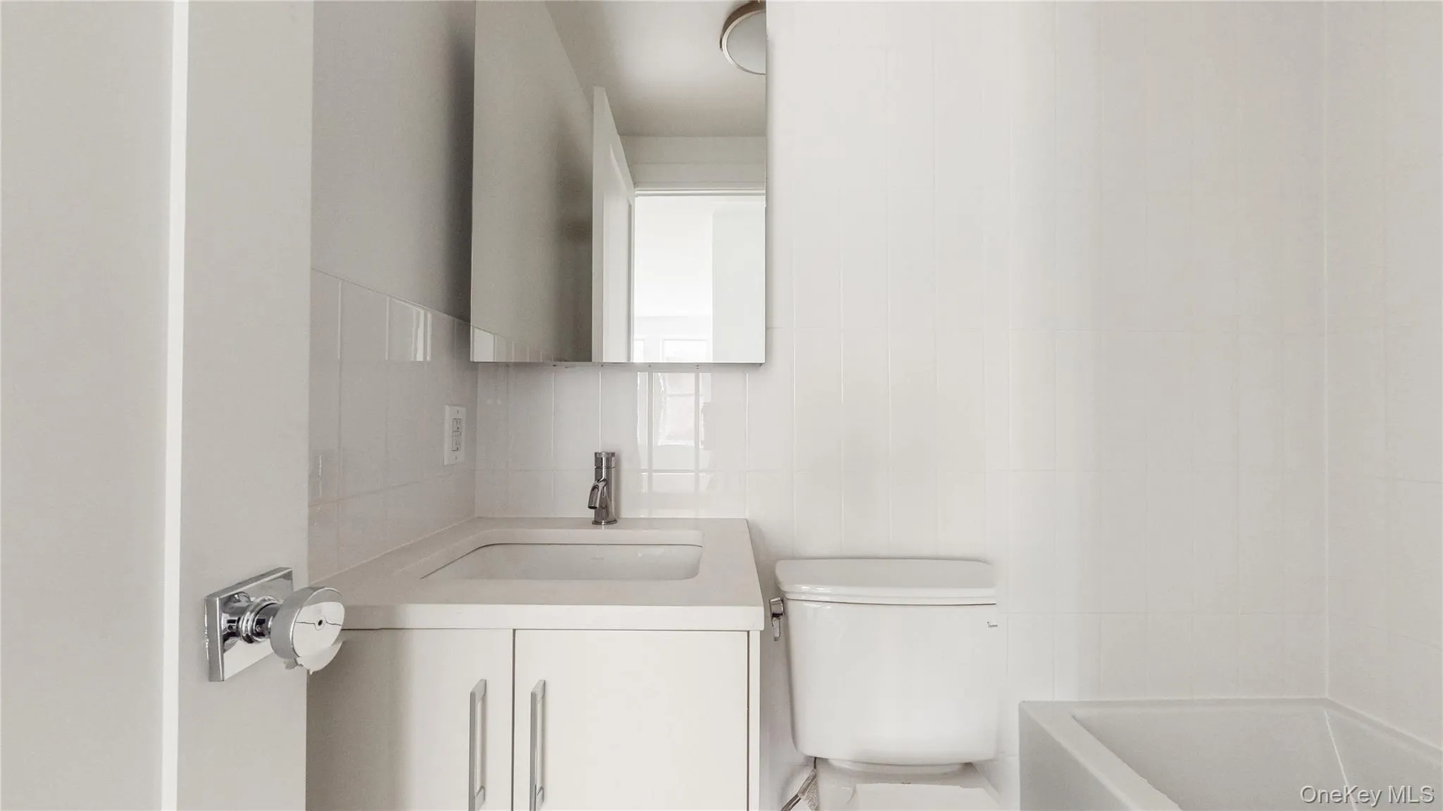 Bathroom featuring a white vanity with integrated sink, chrome faucet, and a wall-mounted mirrored cabinet Bathroom featuring a white vanity with integrated sink, chrome faucet, and a wall-mounted mirrored cabinet
