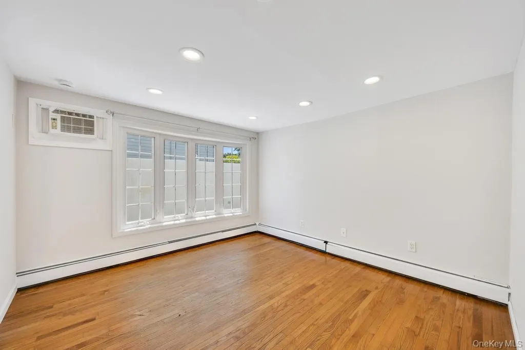 Bay window with white trim, wood-finish flooring, recessed lighting, and a wall-mounted air conditioning unit Bay window with white trim, wood-finish flooring, recessed lighting, and a wall-mounted air conditioning unit